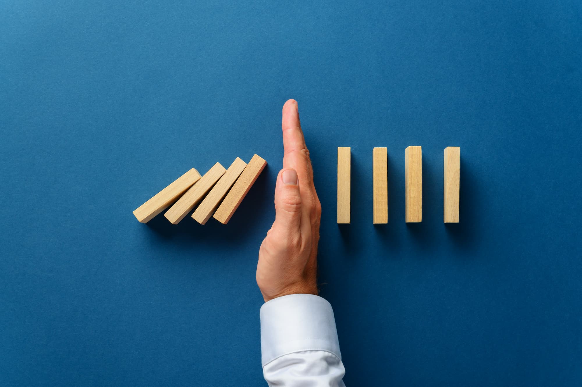man's hand stopping dominoes before they fall