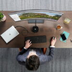 Overhead-Mann im Anzug sitzt am Holzschreibtisch HP-Laptop gebogener Monitor