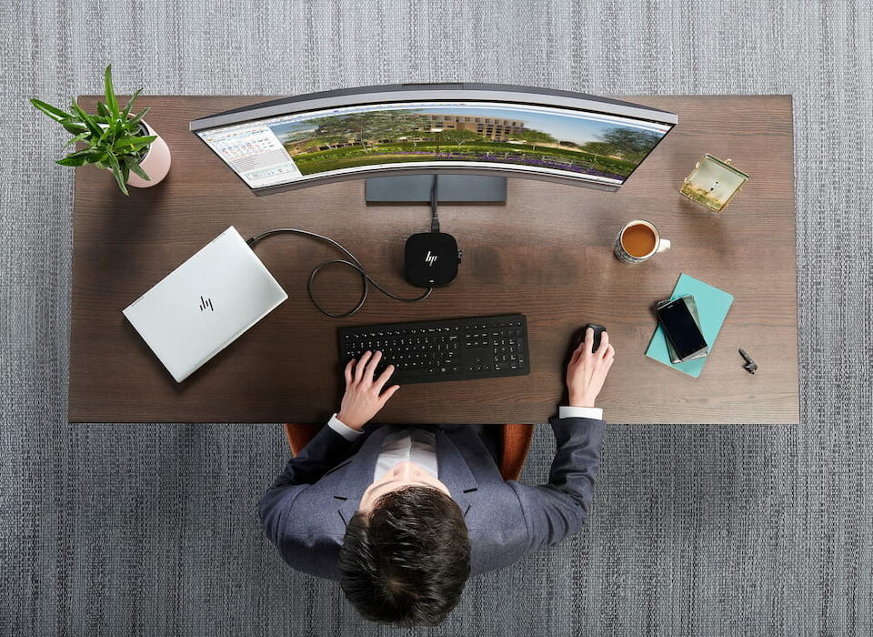 Overhead-Mann im Anzug sitzt am Holzschreibtisch HP-Laptop gebogener Monitor