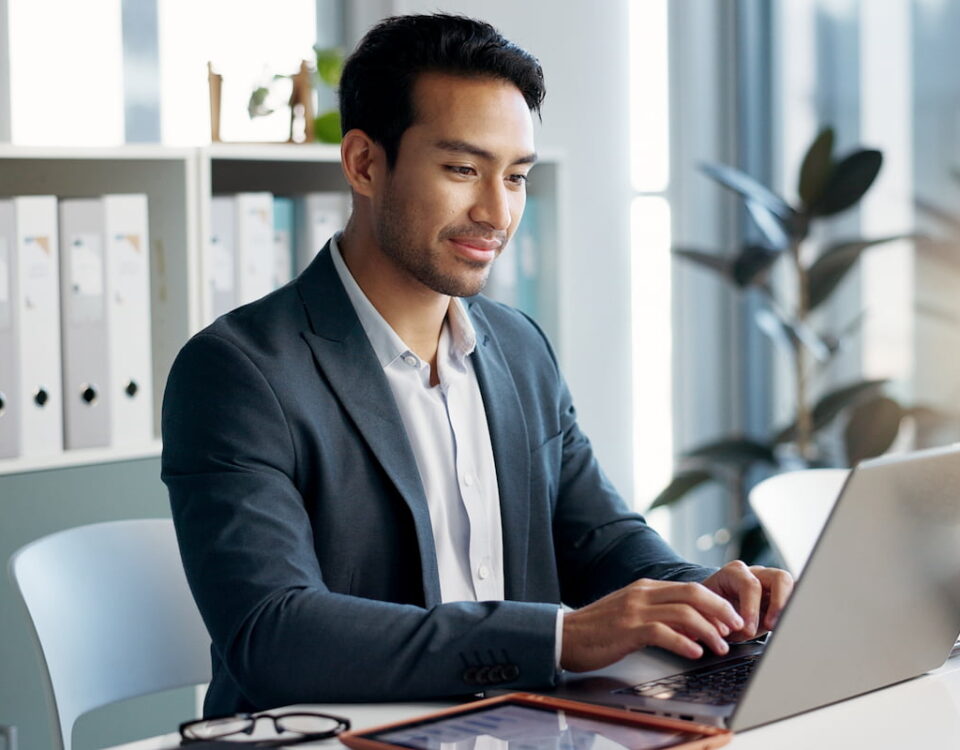 Ein Mann, der in einem weißen Bürobereich einen Laptop und ein Tablet benutzt