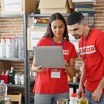 man and woman charity volunteers wearing red and taking inventory with a laptop
