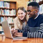 Studierende, die in einer Bibliothek an einem Laptop arbeiten