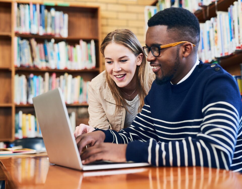 Studierende, die in einer Bibliothek an einem Laptop arbeiten